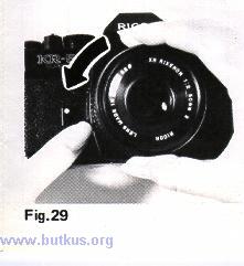 With the other hand, hold the camera body and press Lens Release Lever (16) and turn the lens counterclockwise until it stops (Fig. 28).