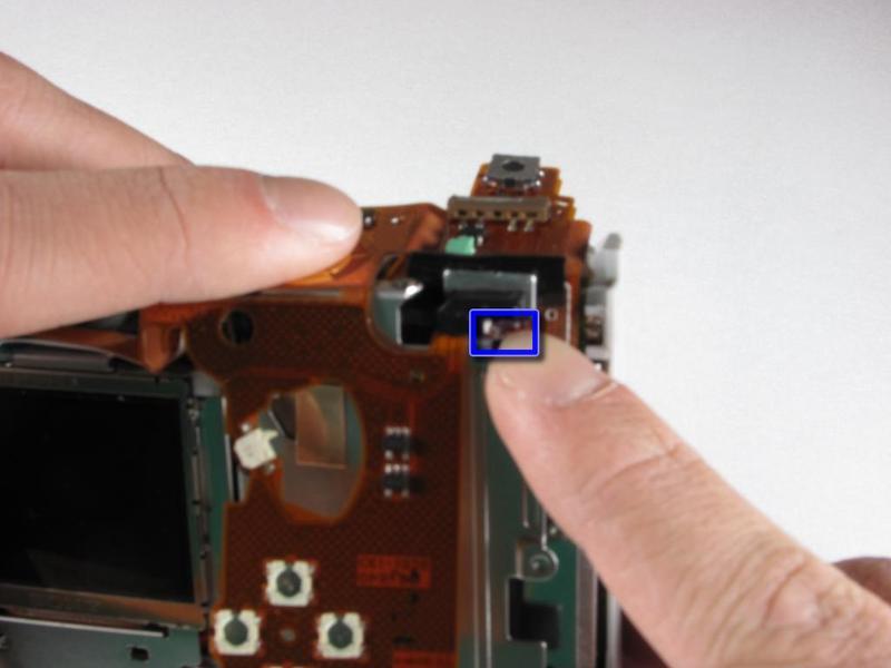 Step 19 Locate the small metal tab that attaches the flex assembly to the upper-right corner of the camera, and