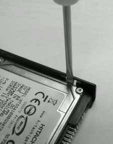Remove the black plastic cover, discard the cover. 19. Using a small flat blade screw driver carefully bend (4) retaining tabs of the hard drive tray slightly outward to release the hard drive.