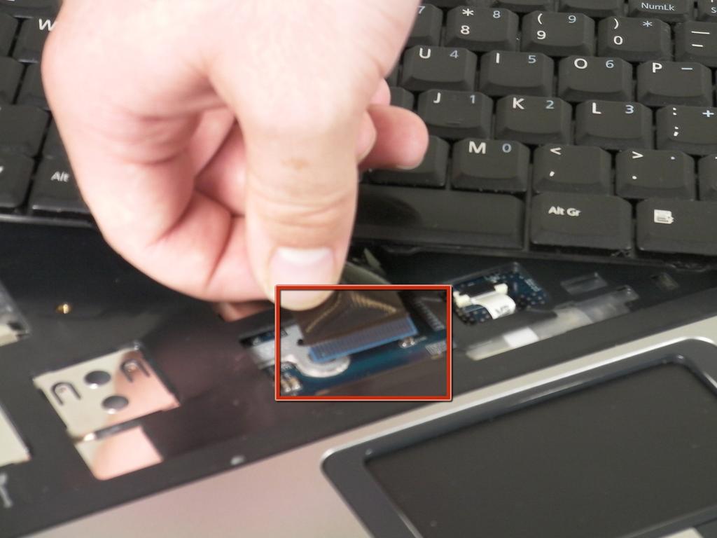 Step 7 Release the catch on the ribbon socket, by sliding the two tabs toward the ribbon, then pull the ribbon, which is located under the keyboard, to detach it