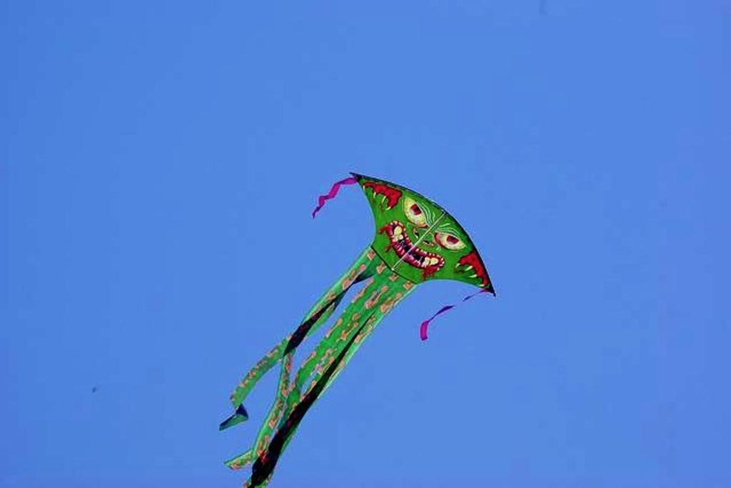 Human: A green monster kite soaring in a sunny sky.