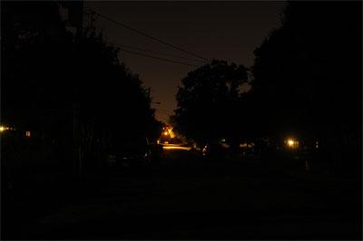 This image shows a dark suburban street, illuminated by nothing but distant street lights.