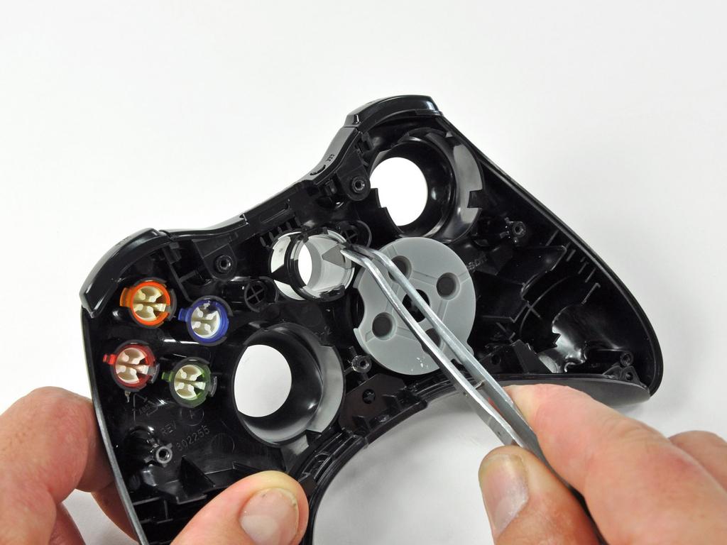 Step 12 Using a pair of tweezers, lift the home button's LED ring out of the front case of the controller. All of the buttons have tabs that correspond to slots in the front case.